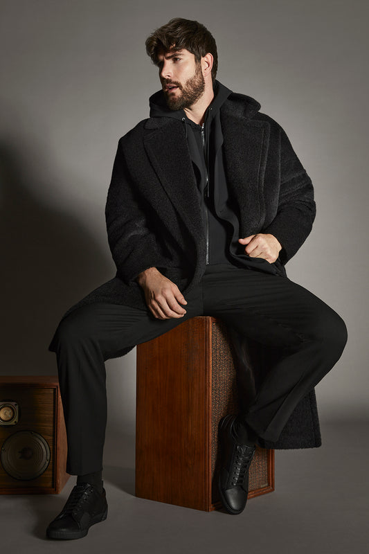 Sentaler Bouclé Alpaca Robe Black Coat in Technical Bouclé Alpaca wool. Seen from front open on male model sitting on retro speakers.