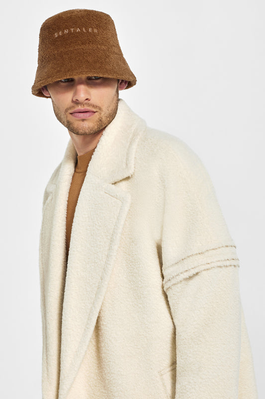 Sentaler Mens Bouclé Alpaca Bucket Hat featured in Bouclé Alpaca and available in Caramel Café. Seen from front above waist on model.